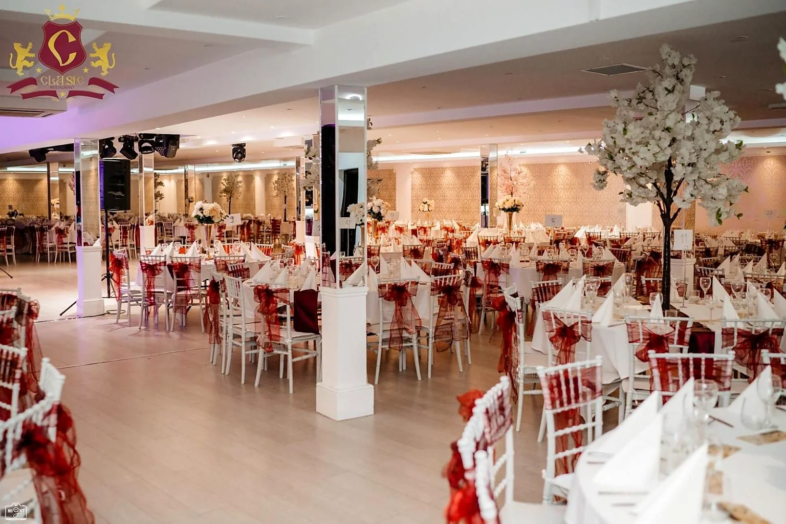 Sala de evenimente Clasic cu mese rotunde, funde bordo pe scaune și aranjamente florale